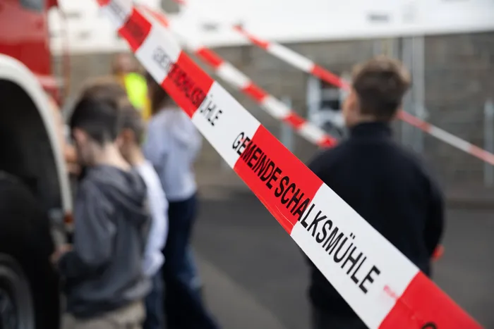 Rot-weißes Absperrband mit der Aufschrift „GEMEINDE SCHALKSMÜHLE“ vor einer Gruppe von Kindern und einem roten Fahrzeug.