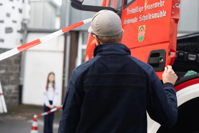 Ein Mann in dunkler Jacke und Kappe steht an einem roten Feuerwehrwagen der Freiwilligen Feuerwehr Schalksmühle bei einer Übung zum Thema „Toter Winkel“.