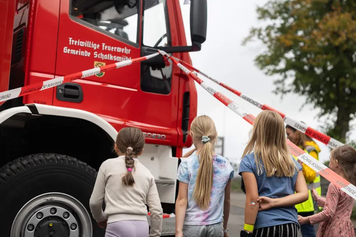 Kinder stehen vor einem roten Feuerwehrauto, das durch rot-weißes Absperrband markiert ist.
