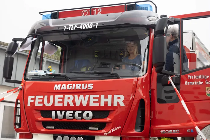 Ein rotes Magirus-Feuerwehrfahrzeug, in dessen Fahrersitz ein Mädchen sitzt.