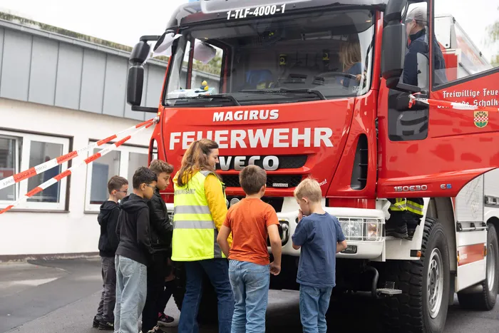 Eine Gruppe von Kindern steht vor einem roten Feuerwehrfahrzeug bei einer Übung zum Thema toter Winkel.