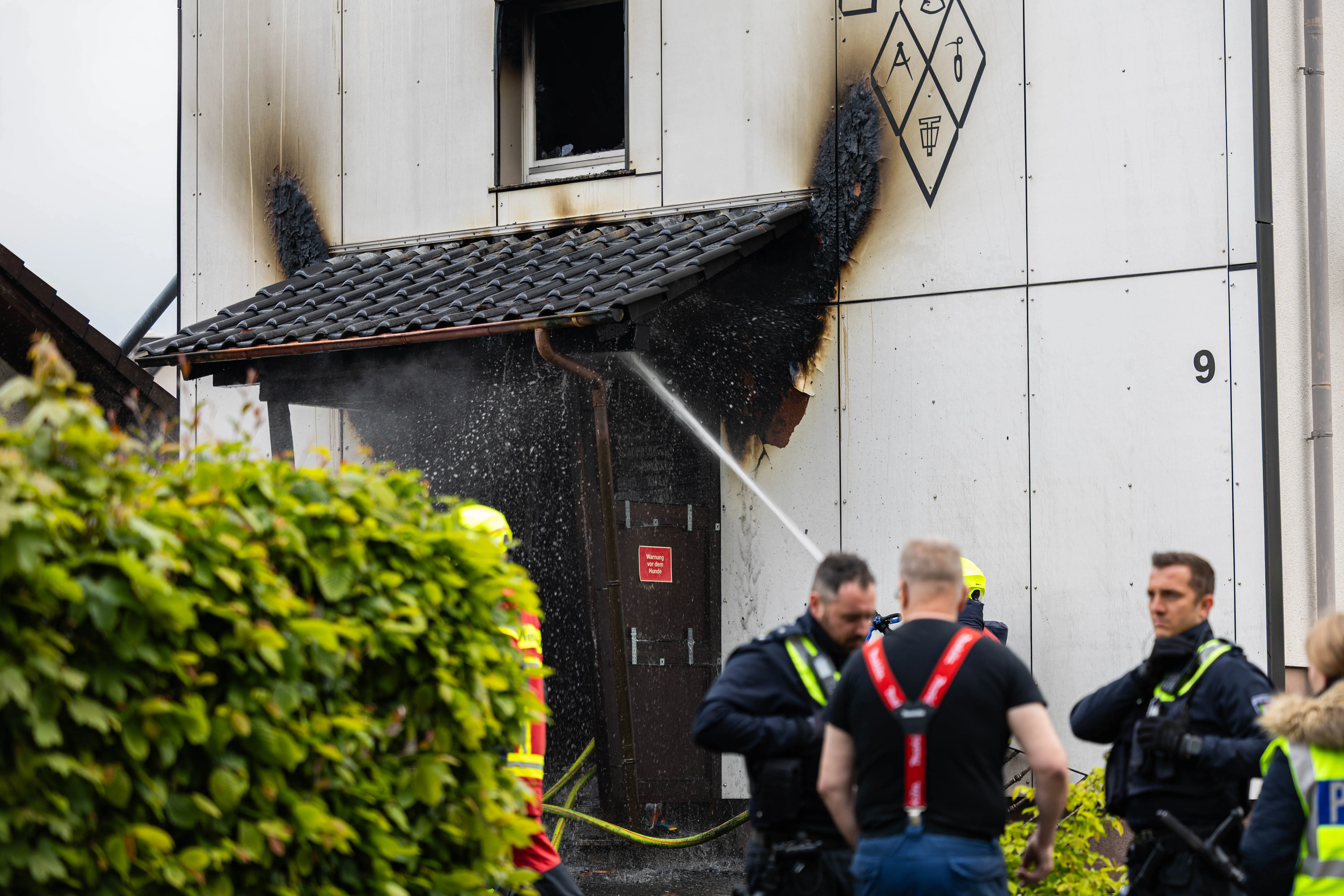 Feuerwehrleute bekämpfen einen Brand an einem Gebäude in der Gartenstraße in Kierspe. Rauch quillt aus einem beschädigten Bereich der Fassade.