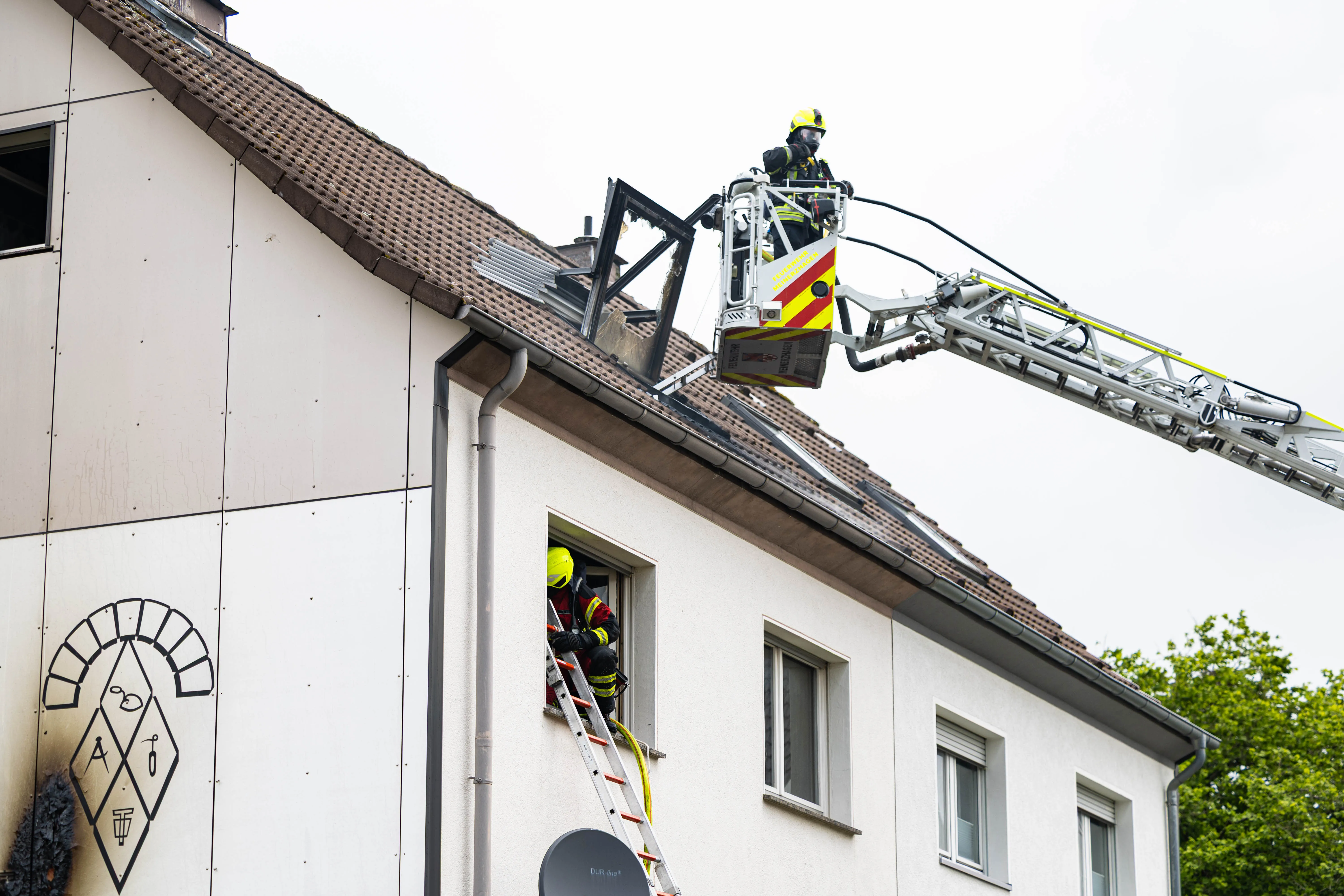 Feuerwehrleute arbeiten an einem Mehrfamilienhaus mit einer Drehleiter, während Rauch aus einem Fenster dringt.