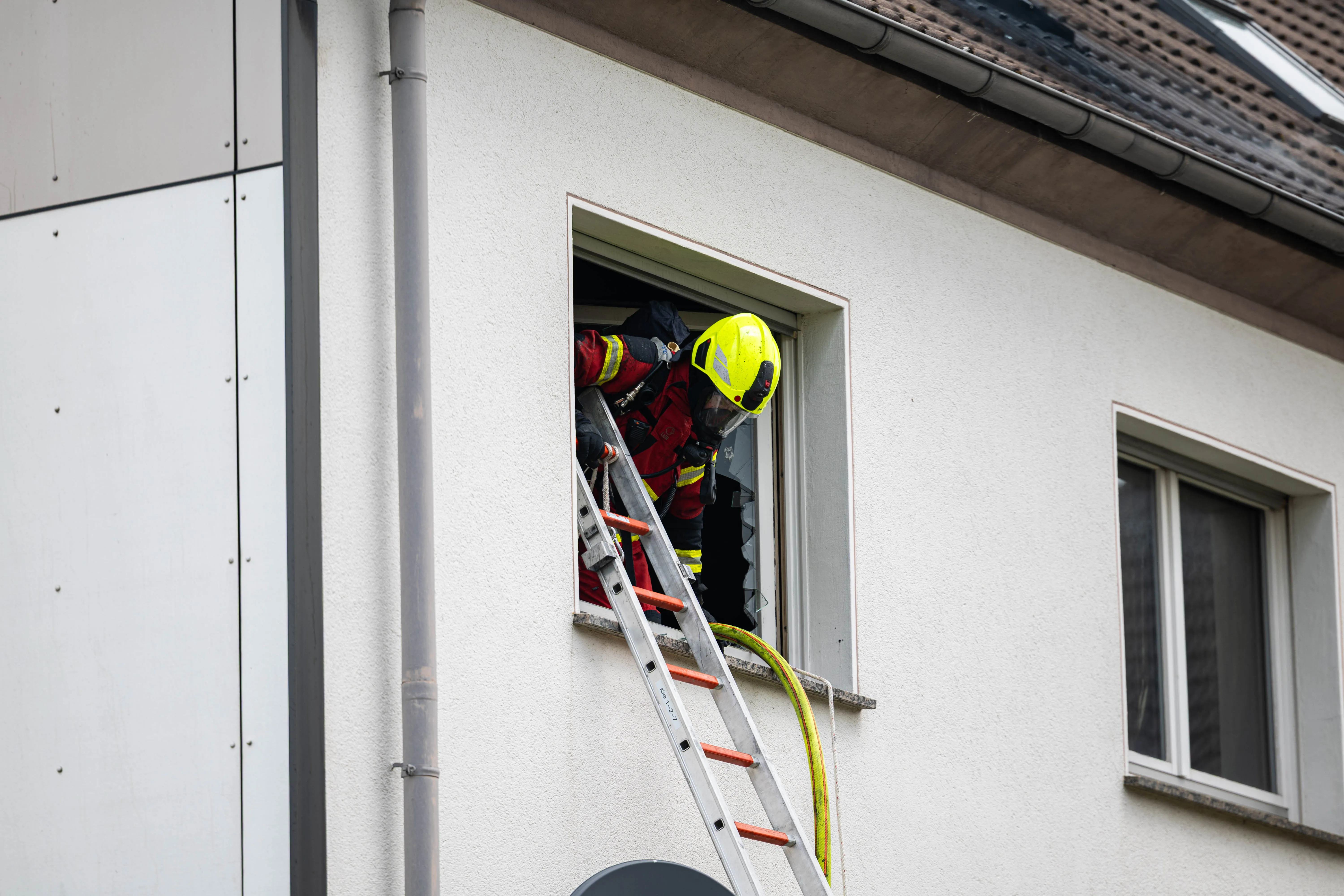 Feuerwehrmann in voller Montur klettert mit einer Leiter in ein Fenster eines hellen Gebäudes während eines Einsatzes in der Gartenstraße.