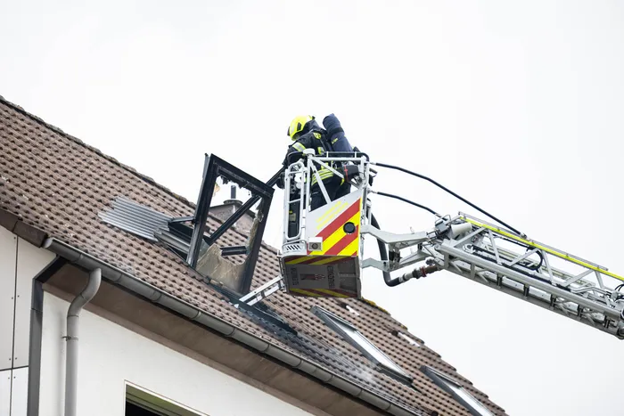 Feuerwehrmann in einer Hebebühne arbeitet an einem beschädigten Dach, während ein weiteres Teammitglied im Hintergrund zu sehen ist.