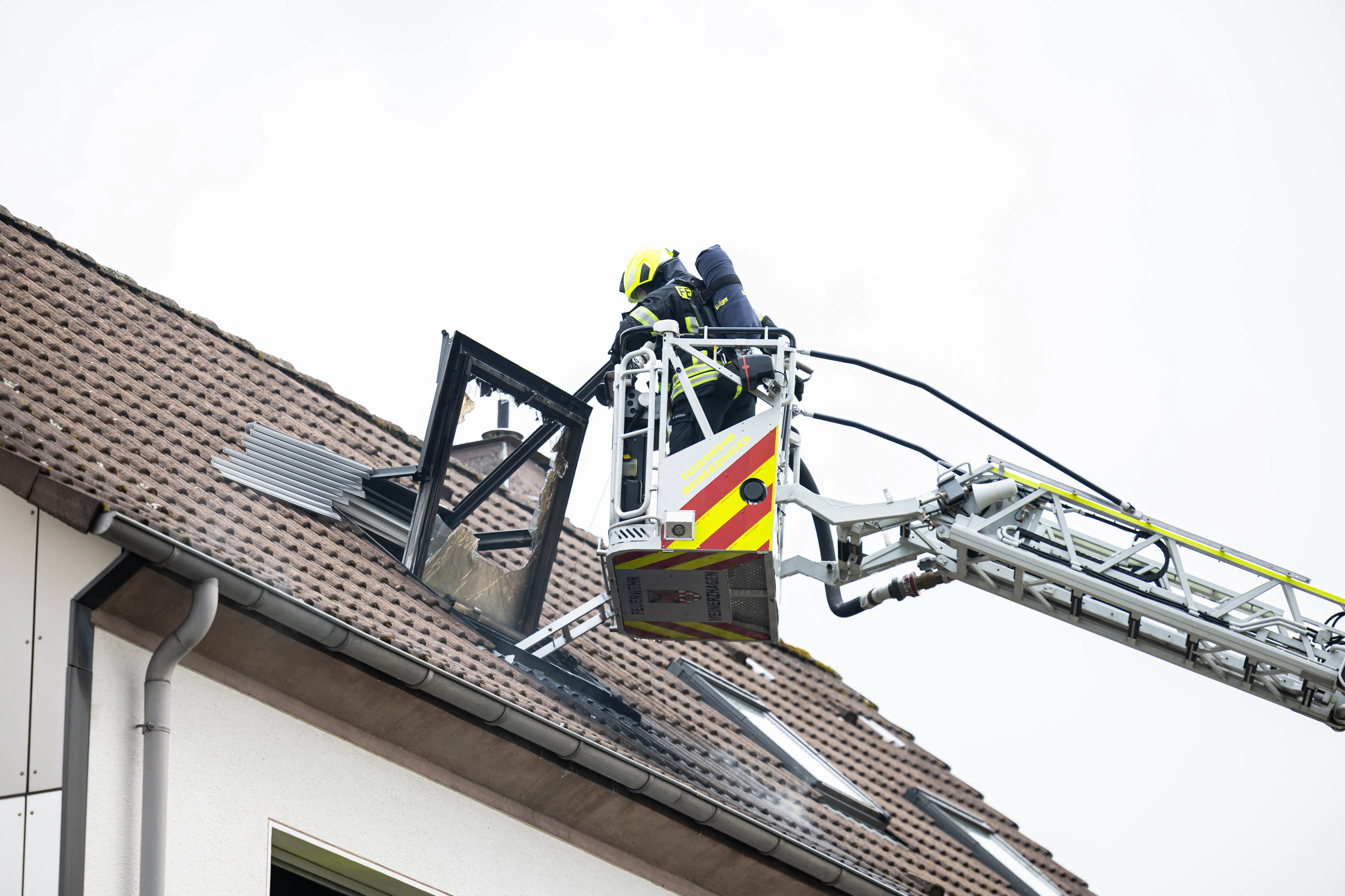 Feuerwehrmann in einer Hebebühne arbeitet an einem beschädigten Dach, während ein weiteres Teammitglied im Hintergrund zu sehen ist.