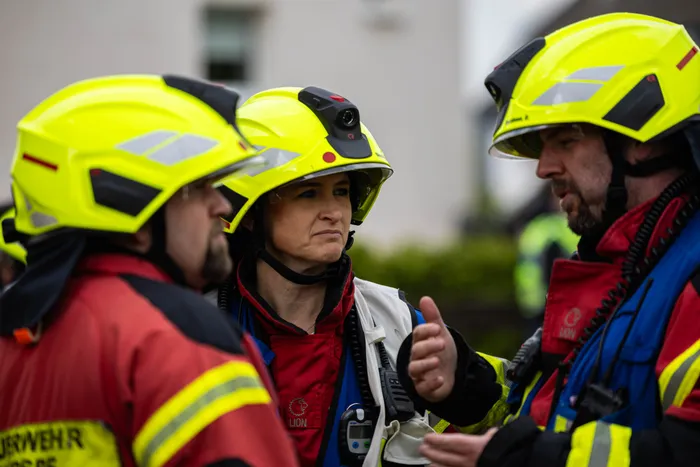 Eine Frau in Schutzkleidung und Helm bespricht mit zwei Feuerwehrleuten die Lage bei einem Einsatz.