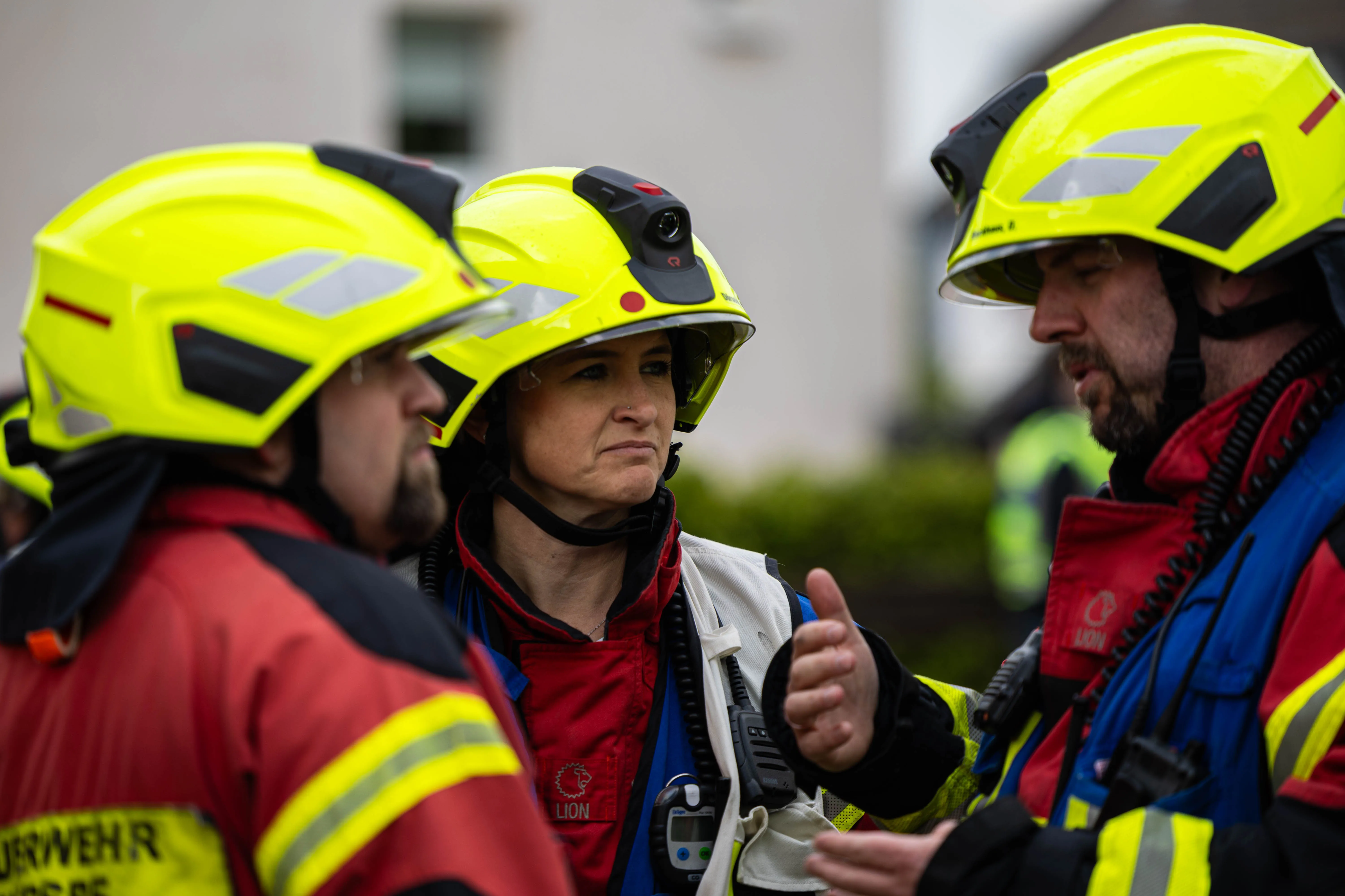 Eine Frau in Schutzkleidung und Helm bespricht mit zwei Feuerwehrleuten die Lage bei einem Einsatz.
