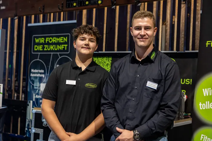 Zwei junge Männer in schwarzen Hemden mit dem Logo „SD FORMEN“ vor einem Banner mit der Aufschrift „WIR FORMEN DIE ZUKUNFT“.