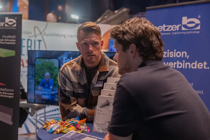 Ein Mann in einer karierten Jacke steht an einem Messestand der Firma Betzer und blickt seinem Gegenüber zu.