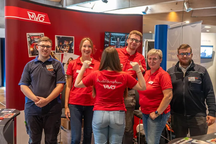 Sechs Personen stehen vor einem roten MVG-Stand, eine davon trägt ein rotes T-Shirt mit der Aufschrift „Ausbildungsteam MVG“.