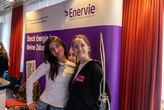 Zwei junge Frauen lächeln vor einem lila Banner der Firma Enervie, das für Ausbildungsangebote wirbt.