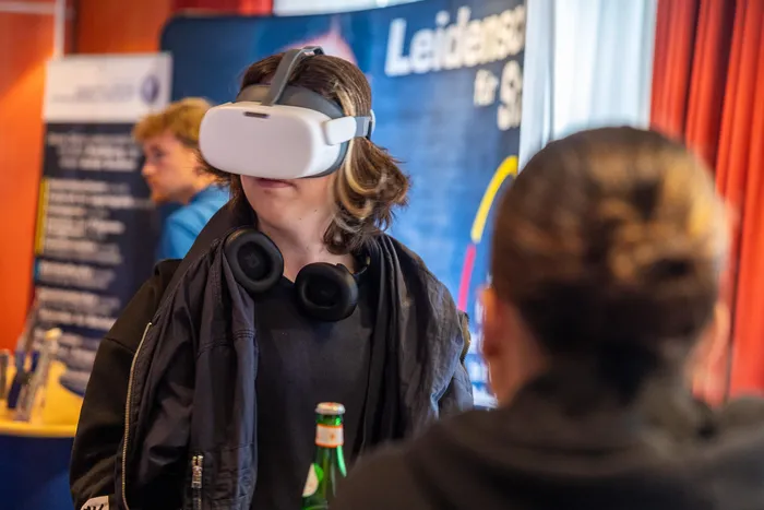 Eine Person trägt ein weißes VR-Headset und schwarze Kopfhörer um den Hals.