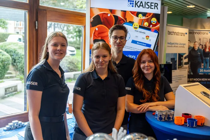Vier junge Menschen in dunklen Poloshirts mit dem „KAISER“-Logo stehen vor einem Messestand auf der ZAK-Ausbildungsmesse.