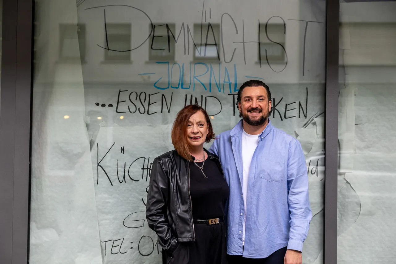 Christiane und Dennis Mouratoglou stehen vor dem Schaufenster ihres neuen Restaurants „Journal“, dessen Eröffnung zur Halveraner Kirmes geplant ist. Im Hintergrund ist die Beschriftung des Schaufensters zu sehen.