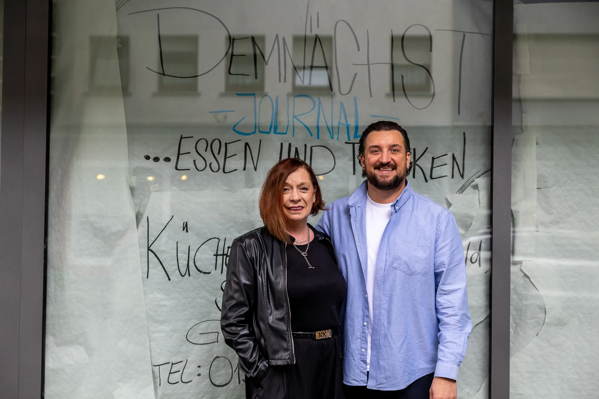 Christiane und Dennis Mouratoglou stehen vor dem Schaufenster ihres neuen Restaurants „Journal“, dessen Eröffnung zur Halveraner Kirmes geplant ist. Im Hintergrund ist die Beschriftung des Schaufensters zu sehen.