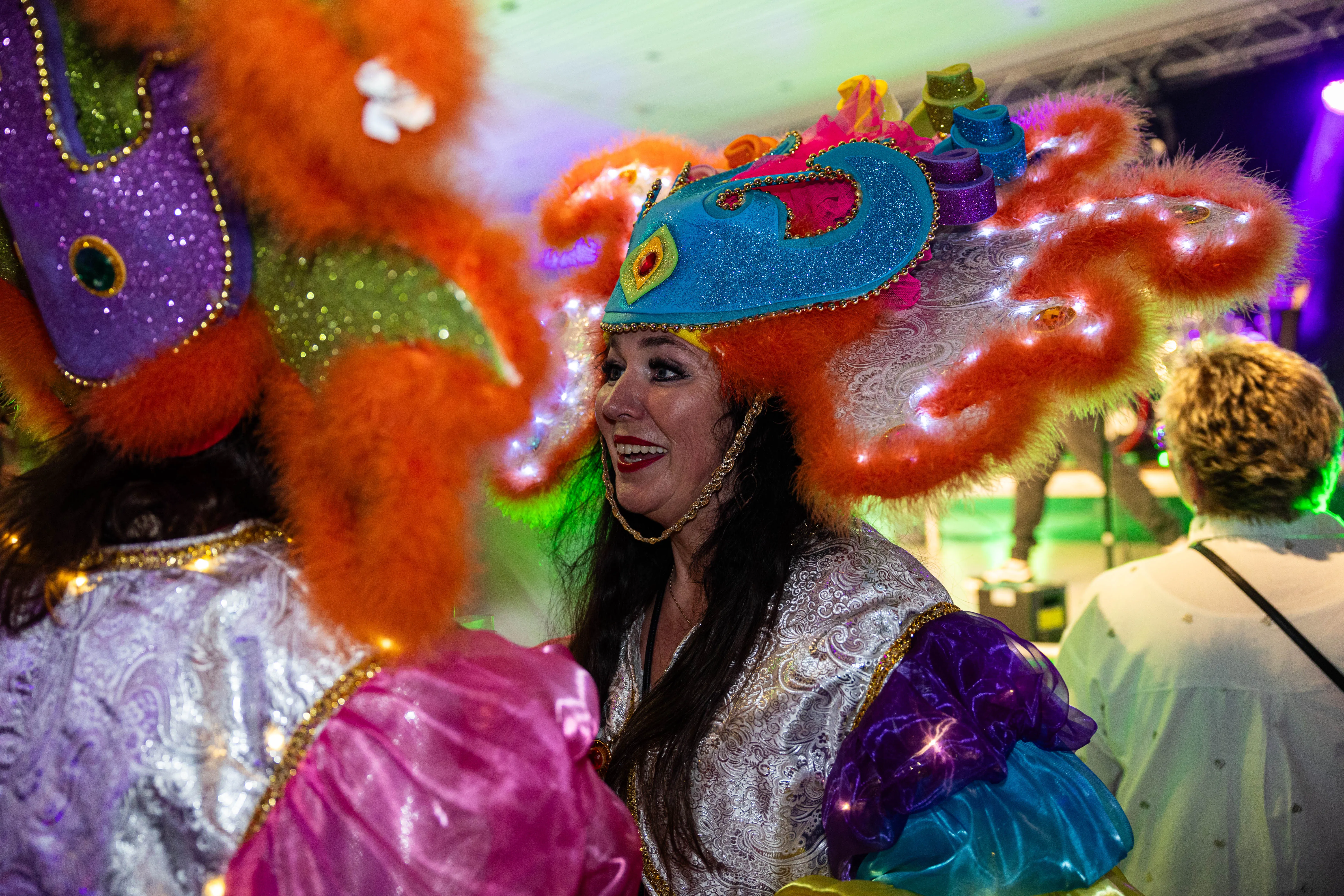 Lachende Frau mit aufwendigem, orangefarbenem Kopfschmuck und festlicher Kleidung inmitten von Menschen in bunten Kostümen auf dem Kölschmusikfestival Valberta Colonia.