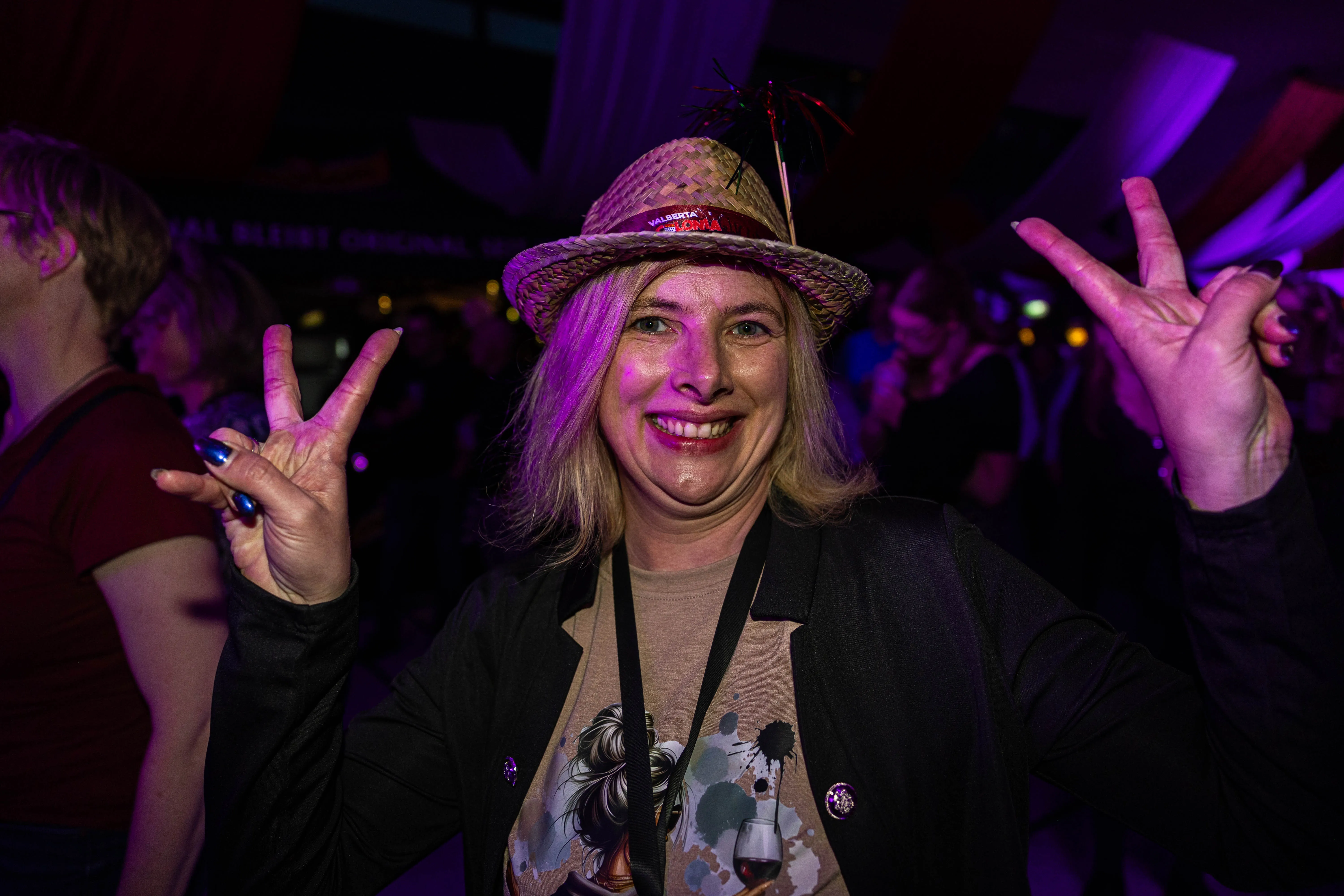 Lachende Frau mit Strohhut und rotem Schmuck zeigt beim Kölschmusikfestival „Valberta Colonia“ die Victory-Geste.