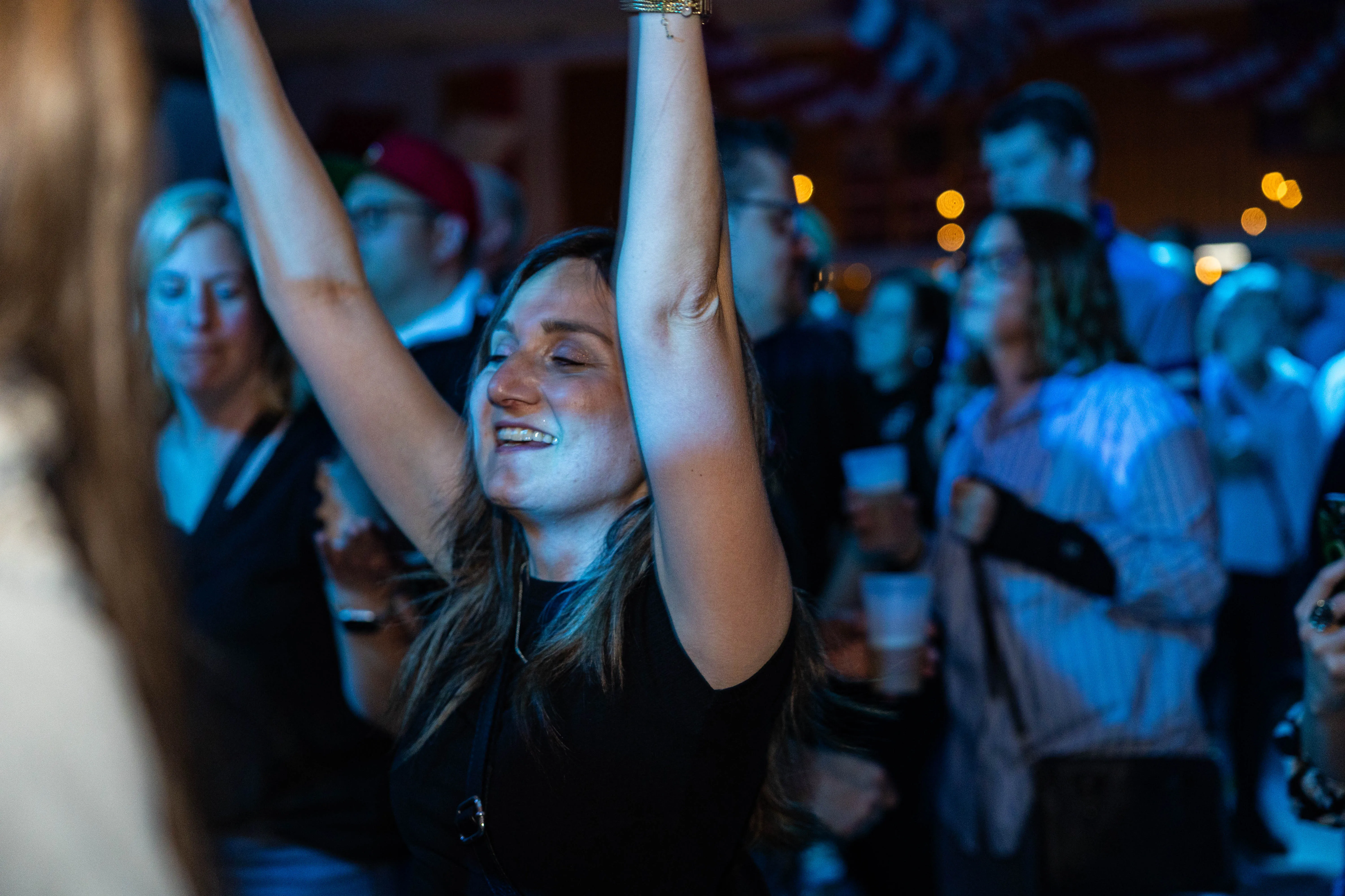 Junge Frau mit geschlossenen Augen und erhobenen Armen tanzt vor einer Menschenmenge auf einem Konzert. Im Hintergrund sind weitere Konzertbesucher und Bühnenlichter zu sehen.