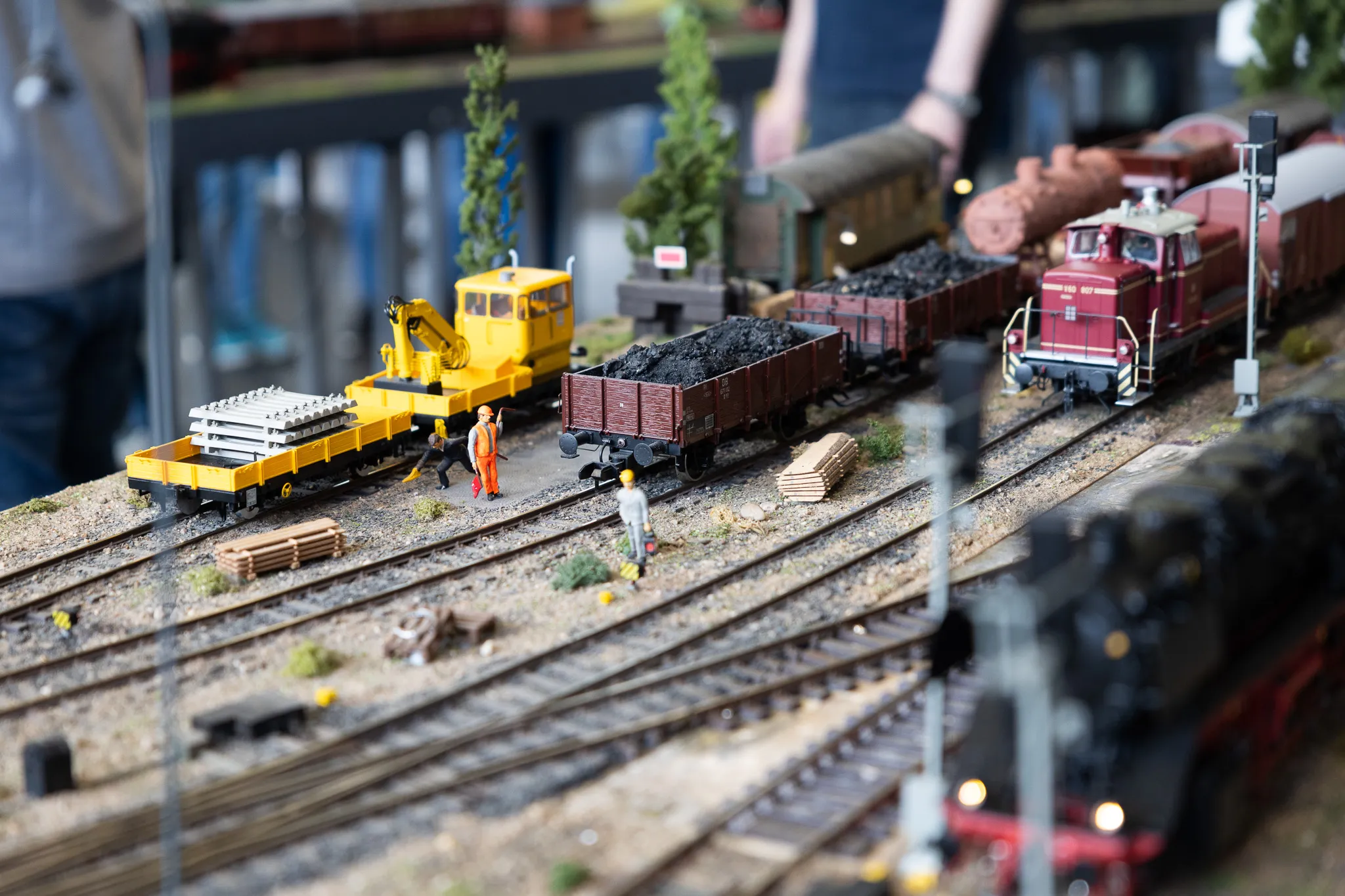 Detailaufnahme einer Miniatur-Eisenbahnanlage mit Gleisen, Waggons, einer Lokomotive und kleinen Figuren, die Arbeiten an der Strecke simulieren.