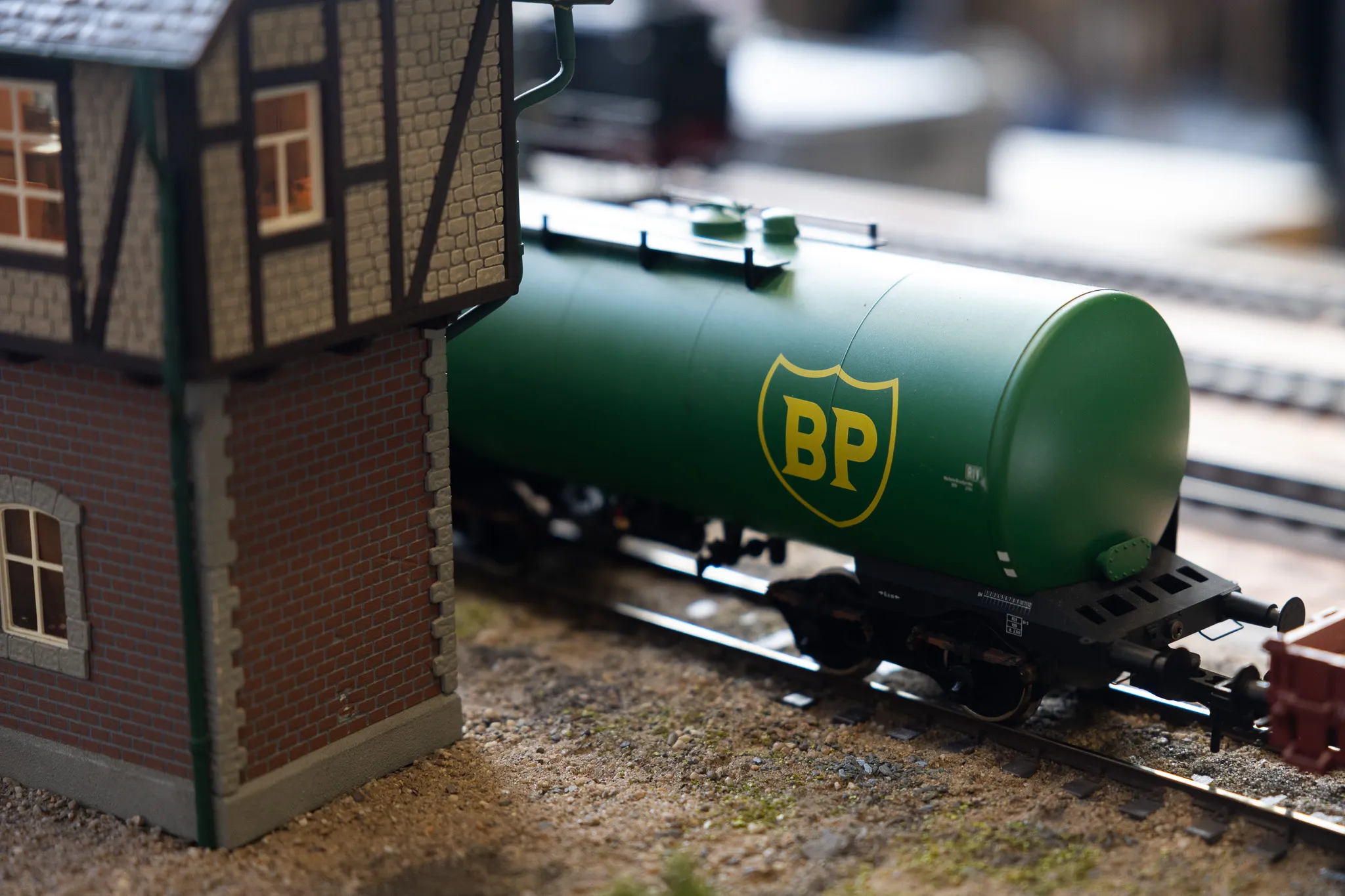 Grüner BP-Tankwagen auf Gleisen einer Modellbahn vor einem kleinen Gebäude.