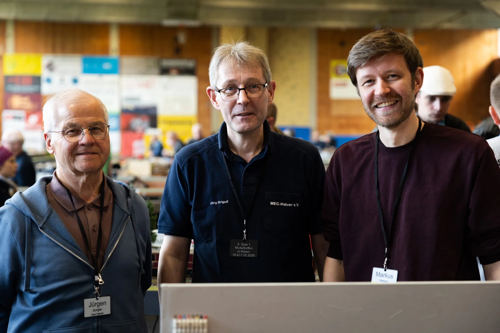 Drei Männer stehen nebeneinander vor einem Tisch mit Modellbahnzubehör. Von links: Jürgen, Jörg Briggull und Markus, alle mit Namensschildern.