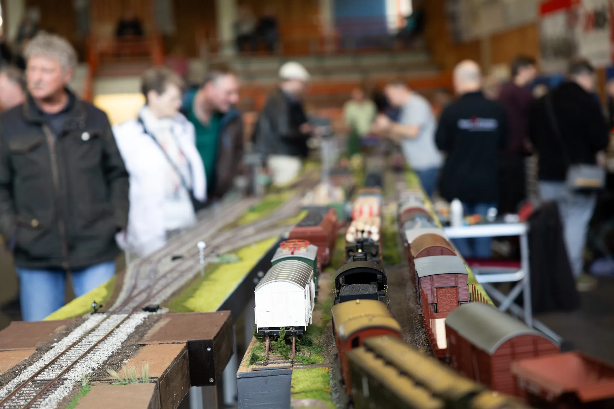 Eine detaillierte Modellbahnanlage mit verschiedenen Waggons steht im Fokus, umgeben von Besuchern einer Ausstellung.