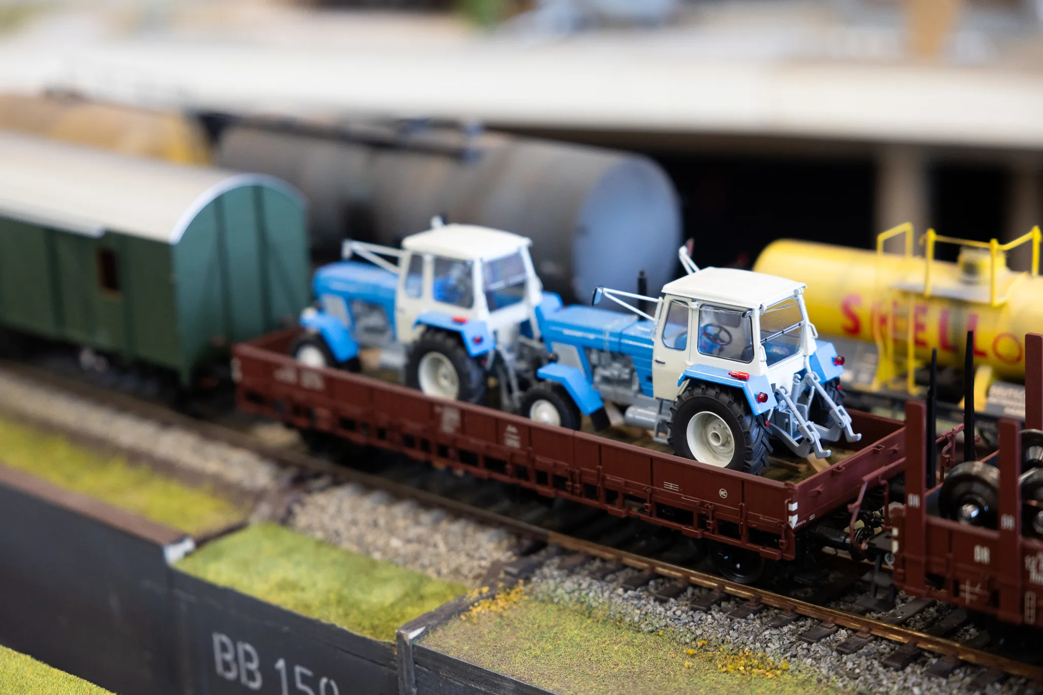 Zwei blaue Modelltraktoren stehen auf einem braunen Güterwagen einer Modellbahn auf Gleisen.