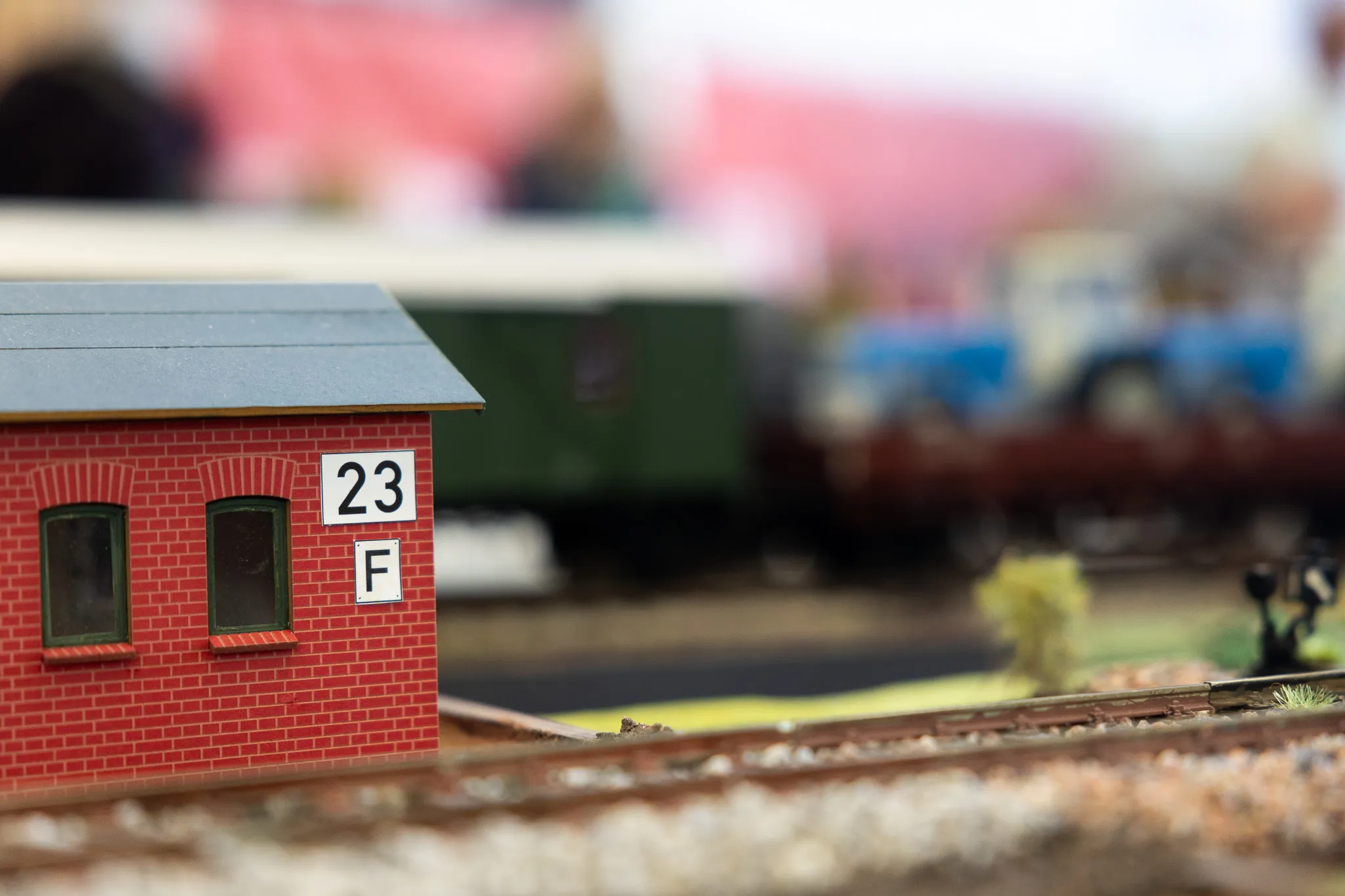 Ein kleines rotes Bahnhofsgebäude mit dem Schild „23 F“ steht neben Gleisen einer Modellbahn.