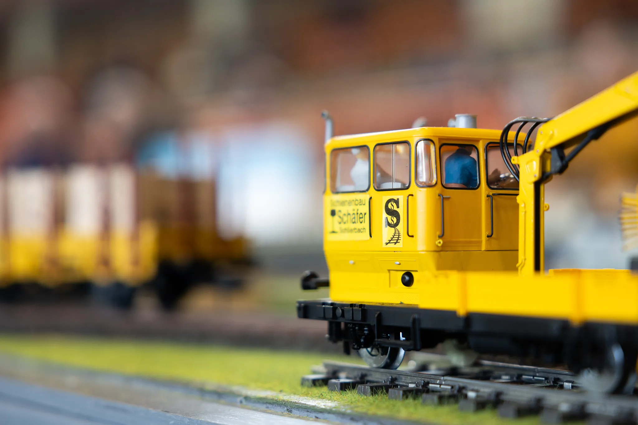 Gelbe Lokomotive einer Modellbahn auf Gleisen, im Hintergrund weitere Waggons unscharf.