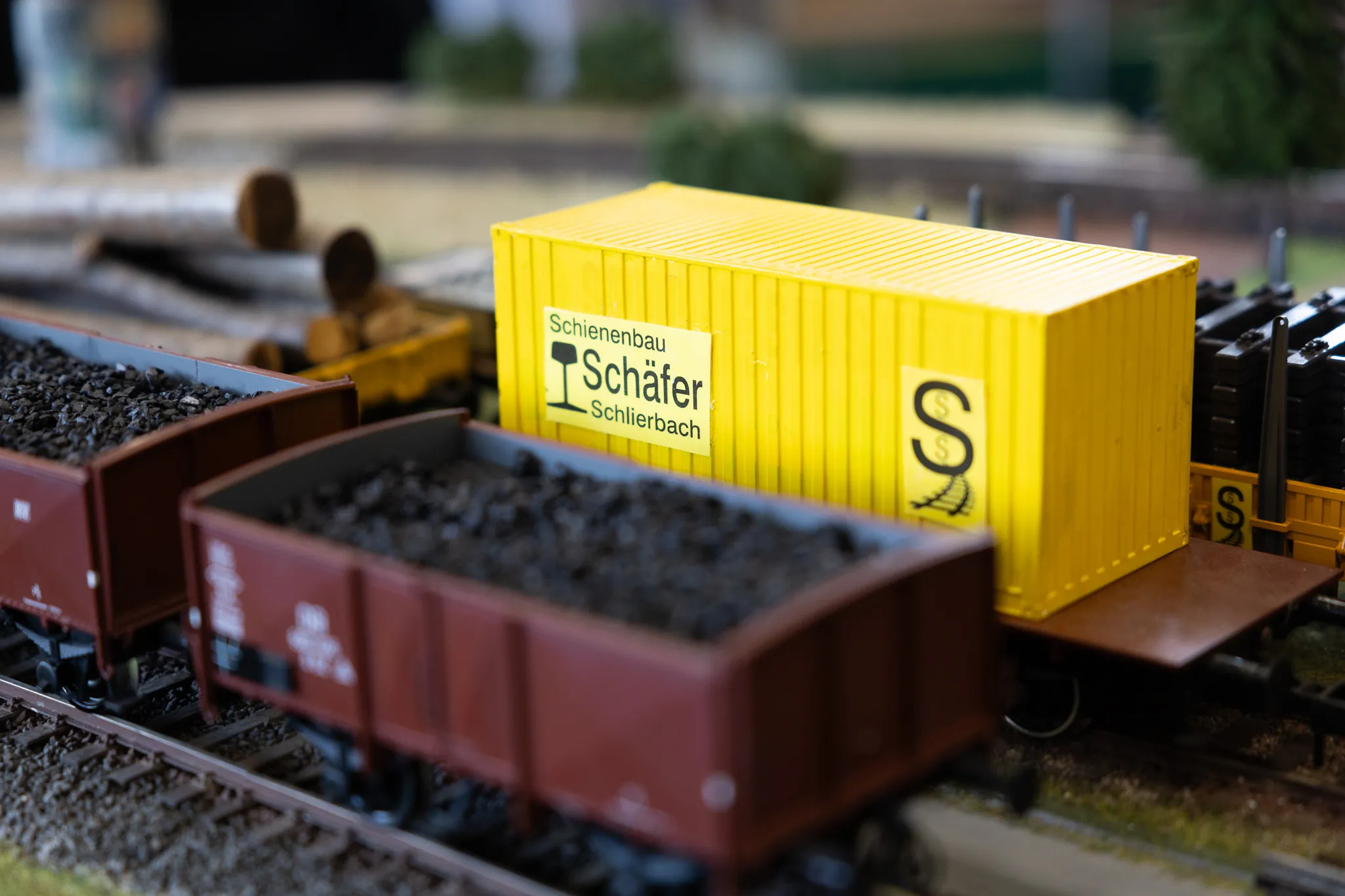 Gelber Container mit dem Schriftzug „Schienenbau Schäfer“ und Kohlewagen auf einer Modellbahn.