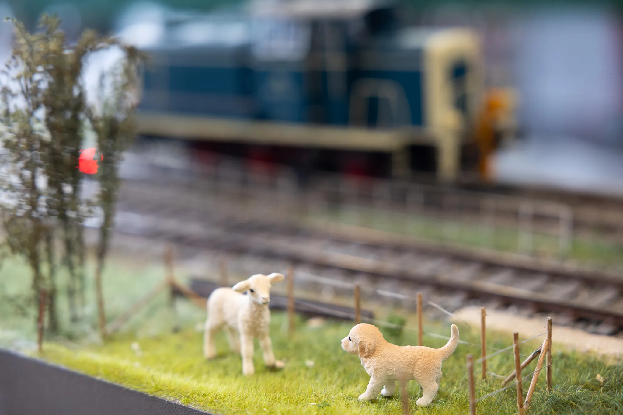 Miniatur-Landschaft mit Schaf, Welpen und einer Modelleisenbahn im Hintergrund.
