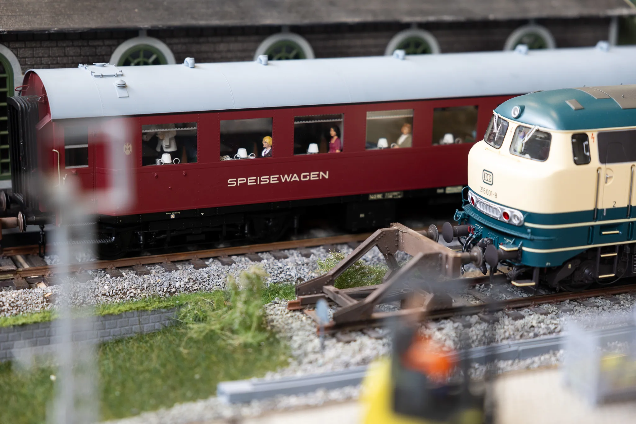 Ein Modellzug mit einem Speisewagen und einer Lokomotive fährt auf Gleisen einer Miniaturlandschaft.