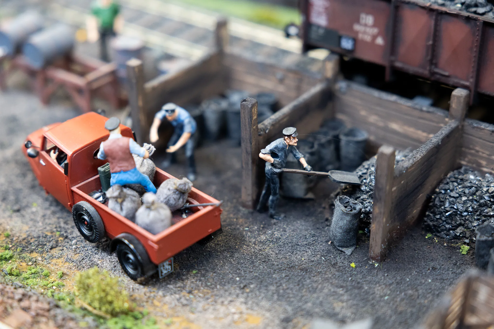 Miniaturfiguren arbeiten auf einer detaillierten Modellbahnanlage, beladen einen roten LKW mit Kohle und schaufeln Kohle in einen Lagerbereich.