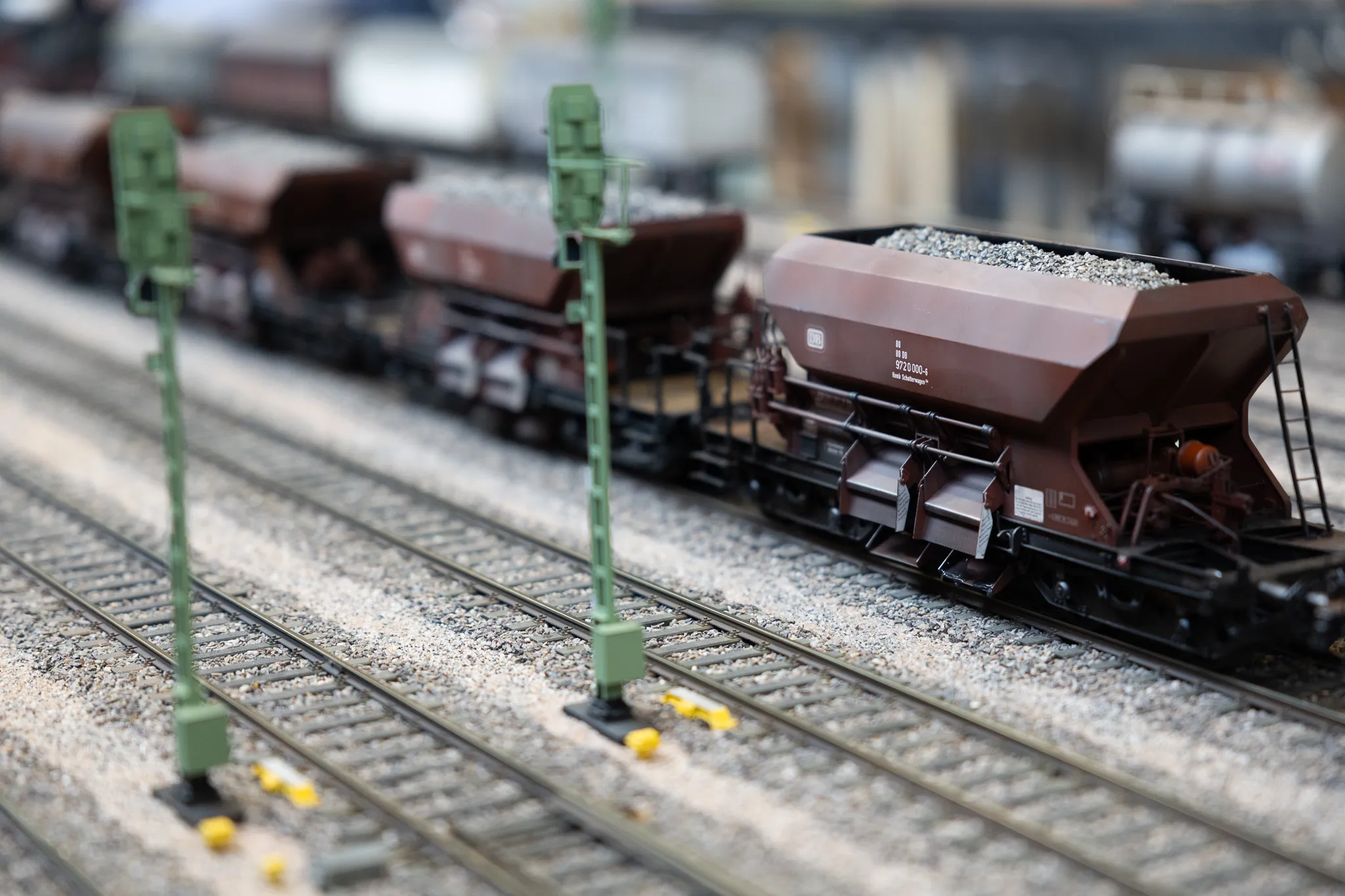 Mehrere braune Güterwaggons einer Modellbahn auf Gleisen, beladen mit Kies.