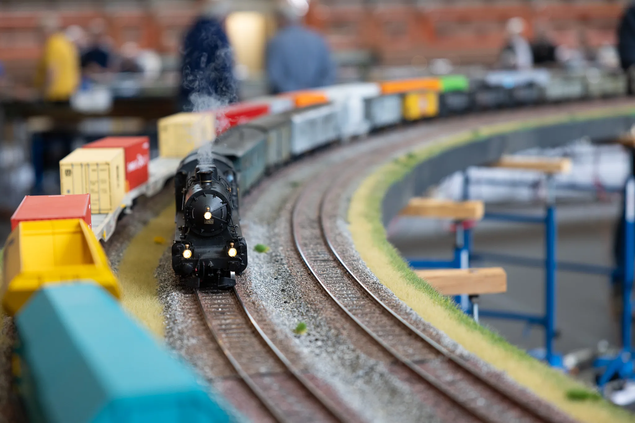 Schwarze Dampflokomotive mit mehreren Waggons auf einer Modellbahn, die sich auf einem ovalen Gleisbett bewegt.