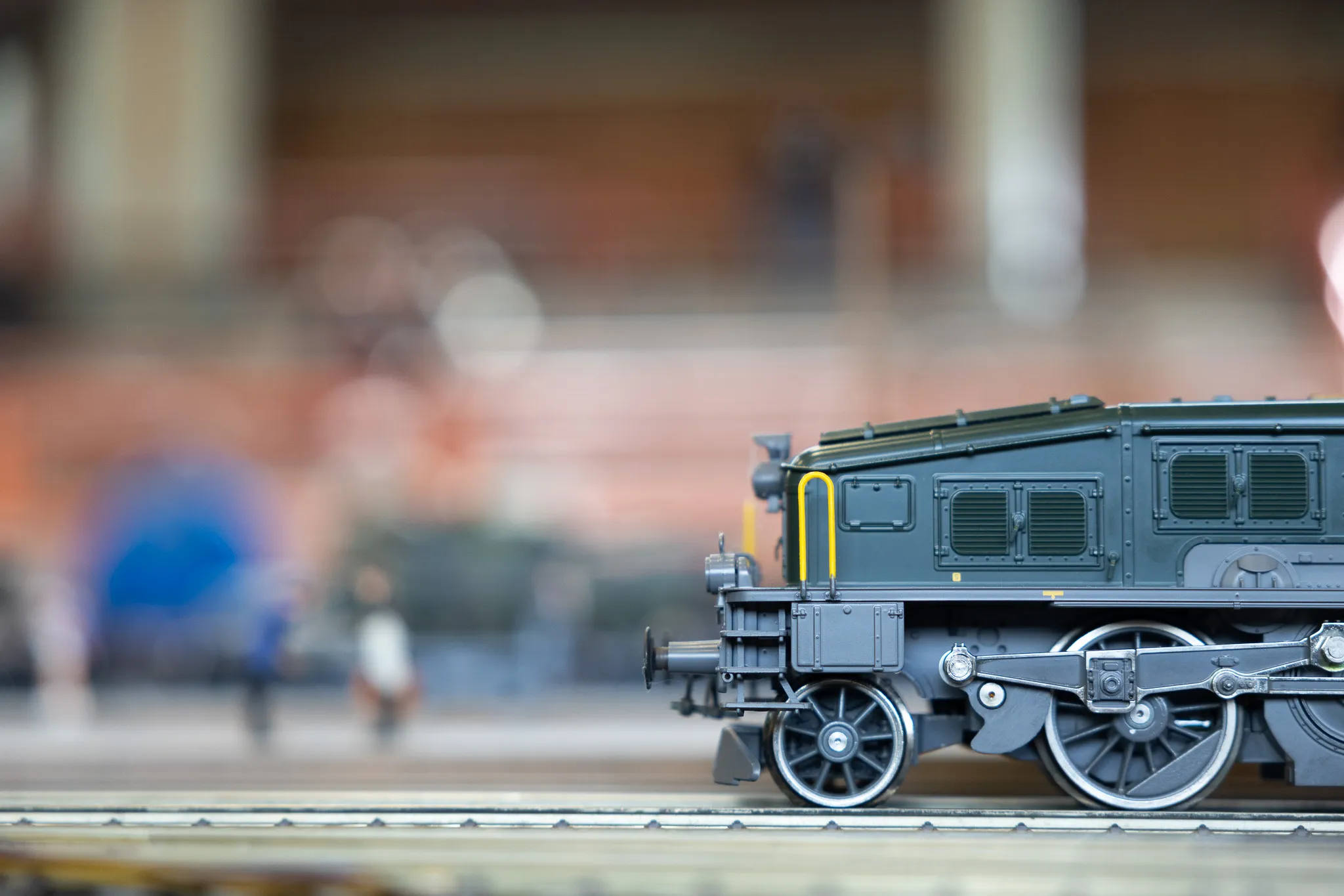 Detailaufnahme einer grauen Lokomotive einer Modellbahn vor unscharfem Hintergrund mit Besuchern.