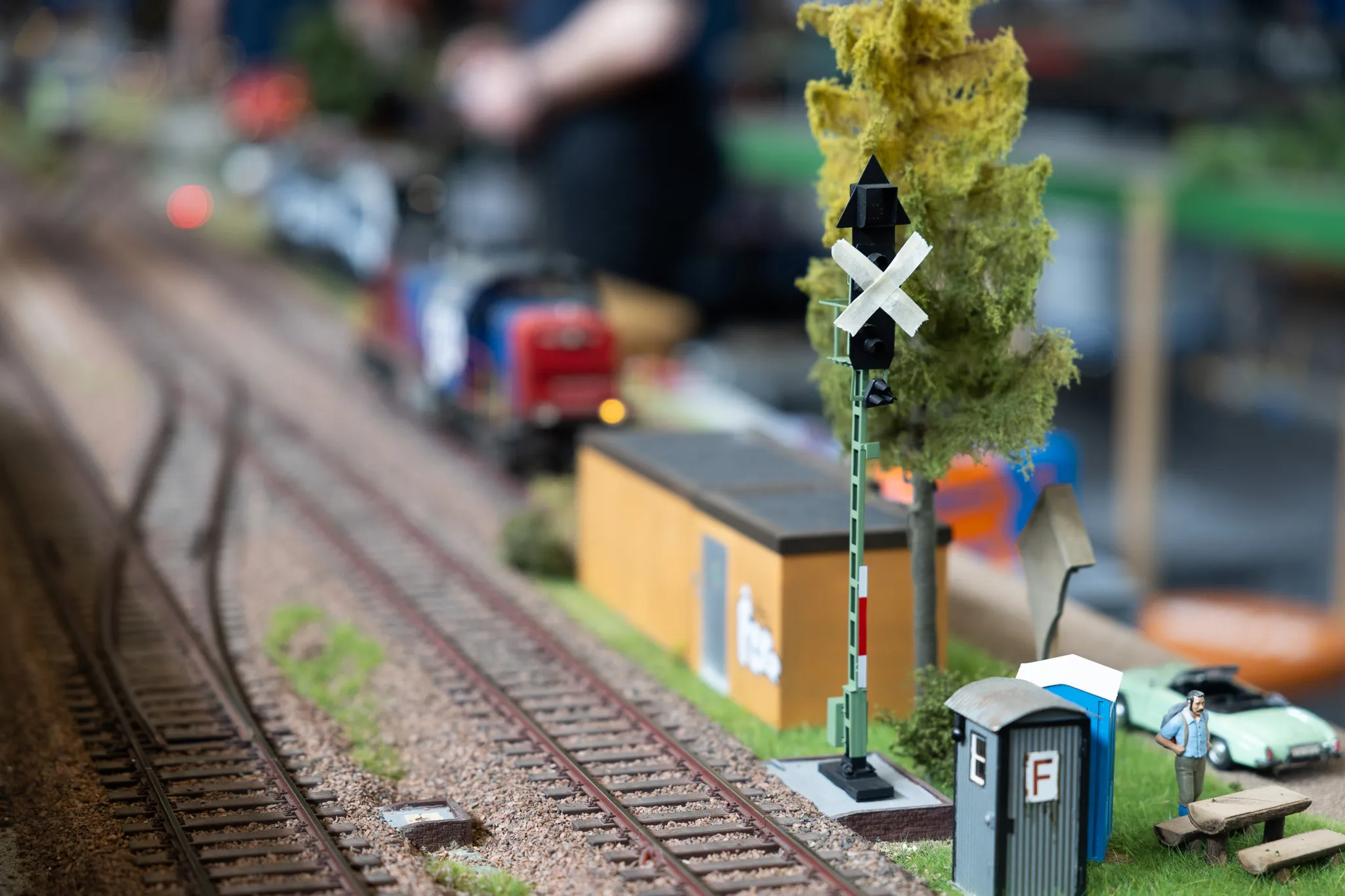 Modellbahn-Gleise mit Schranke und kleinem Wärterhäuschen, daneben eine Miniaturfigur eines Bahnangestellten.