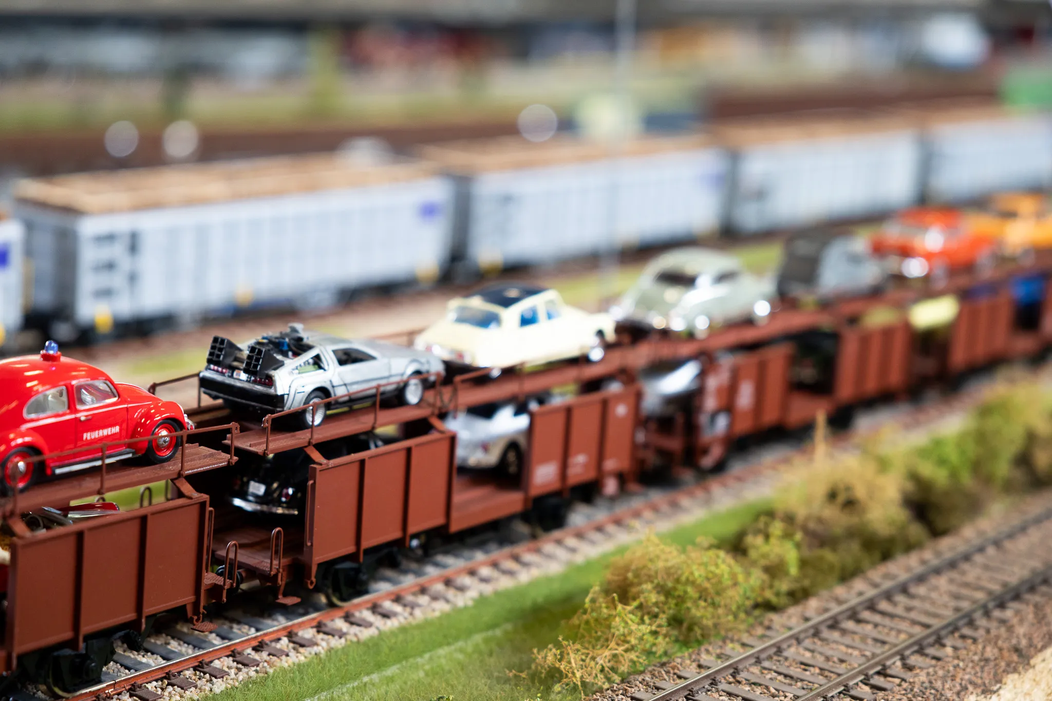 Mehrere rote Güterwaggons transportieren verschiedene Modellautos auf einer Miniatur-Eisenbahnstrecke.