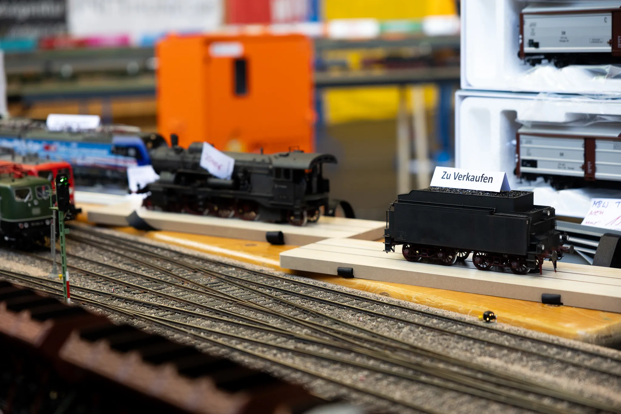 Modellbahn-Ausstellung mit einer Dampflok und Güterwagen auf Gleisen, ein Schild weist auf Verkauf hin.