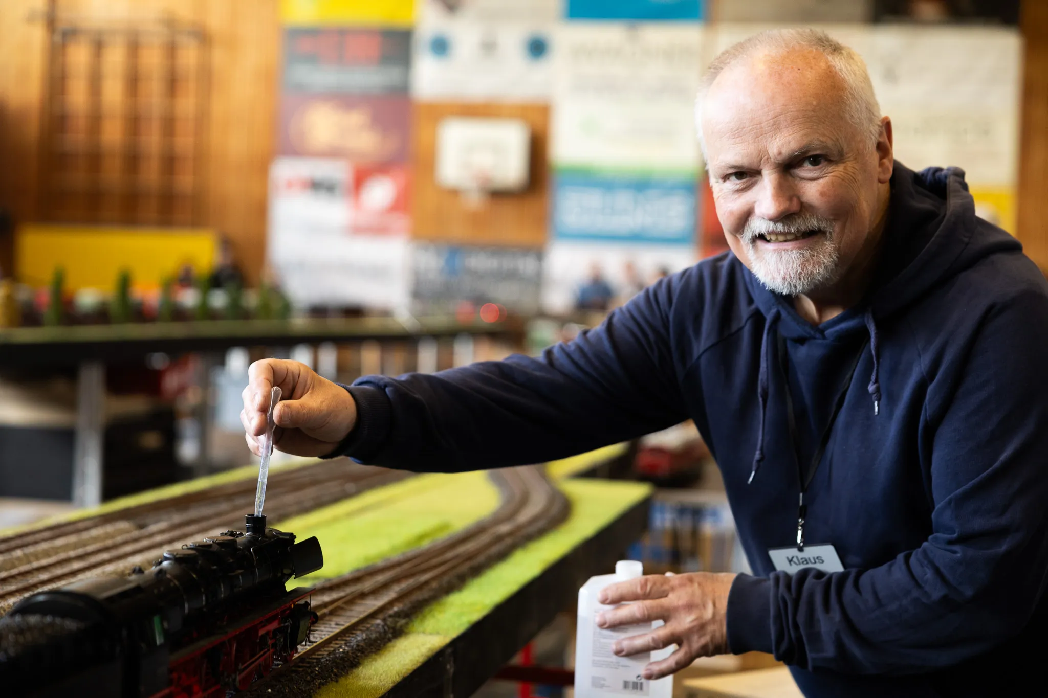 Ein älterer Mann mit Namensschild „Klaus“ betropft eine Modelleisenbahn mit Öl. Im Hintergrund sind weitere Modelle und Ausstellungsstücke zu sehen.
