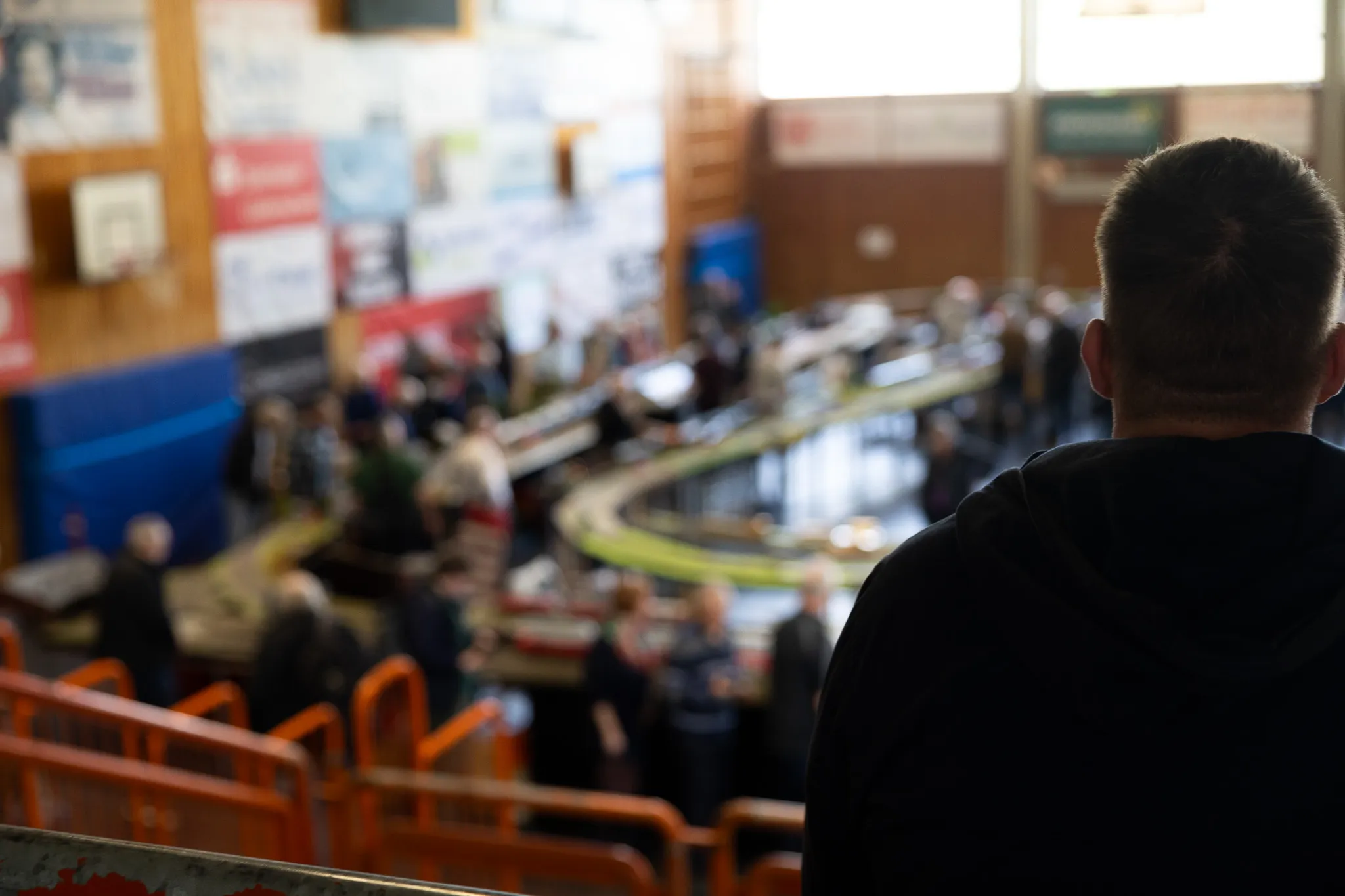 Ein Mann steht mit dem Rücken zum Betrachter und blickt auf eine Modellbahn-Ausstellung mit vielen Besuchern in einer Turnhalle.