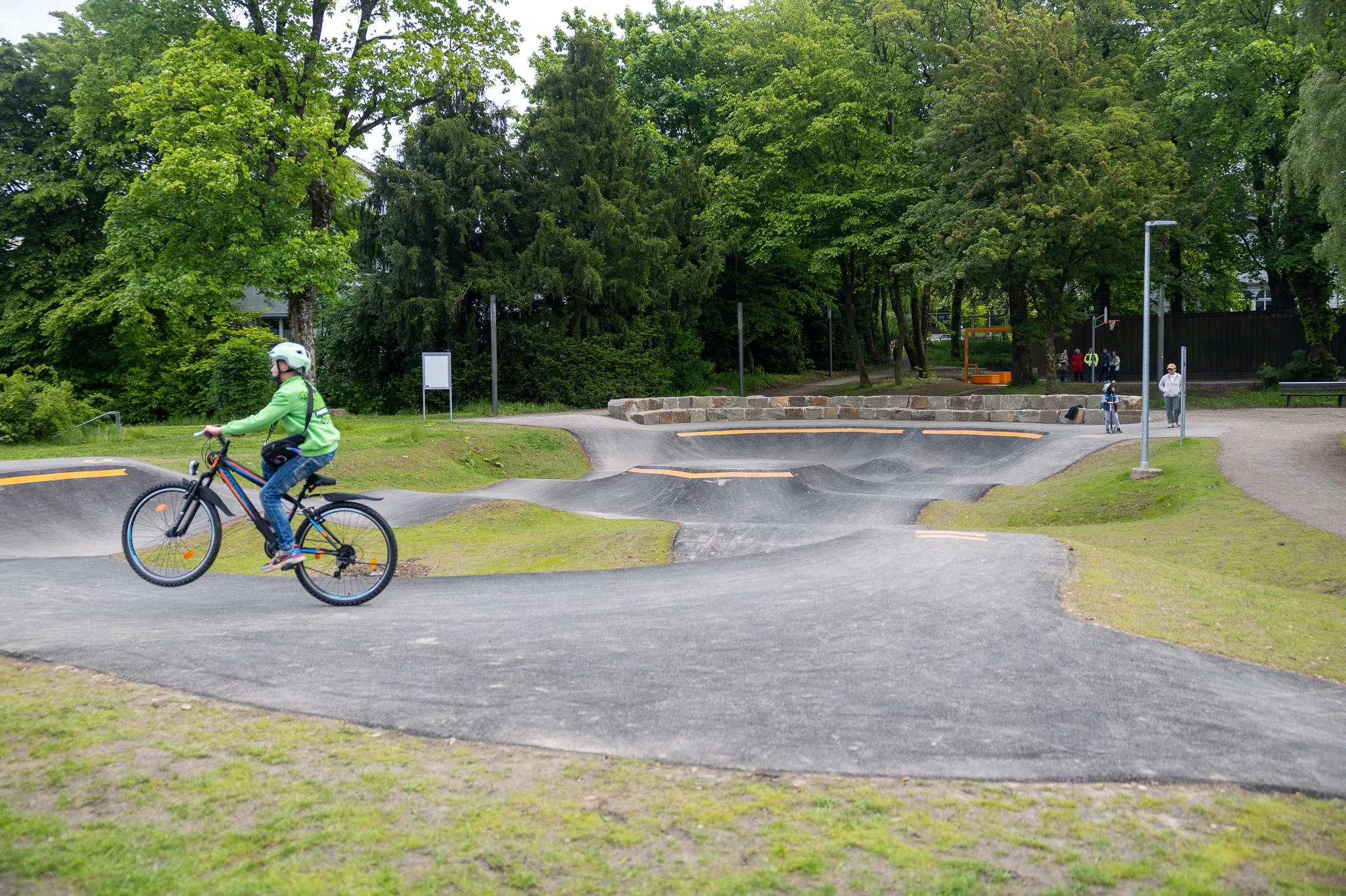 Ein Jugendlicher fährt mit dem Fahrrad auf einem Pumptrack im Lüdenscheider Stadtgarten, während im Hintergrund weitere Personen zu sehen sind.