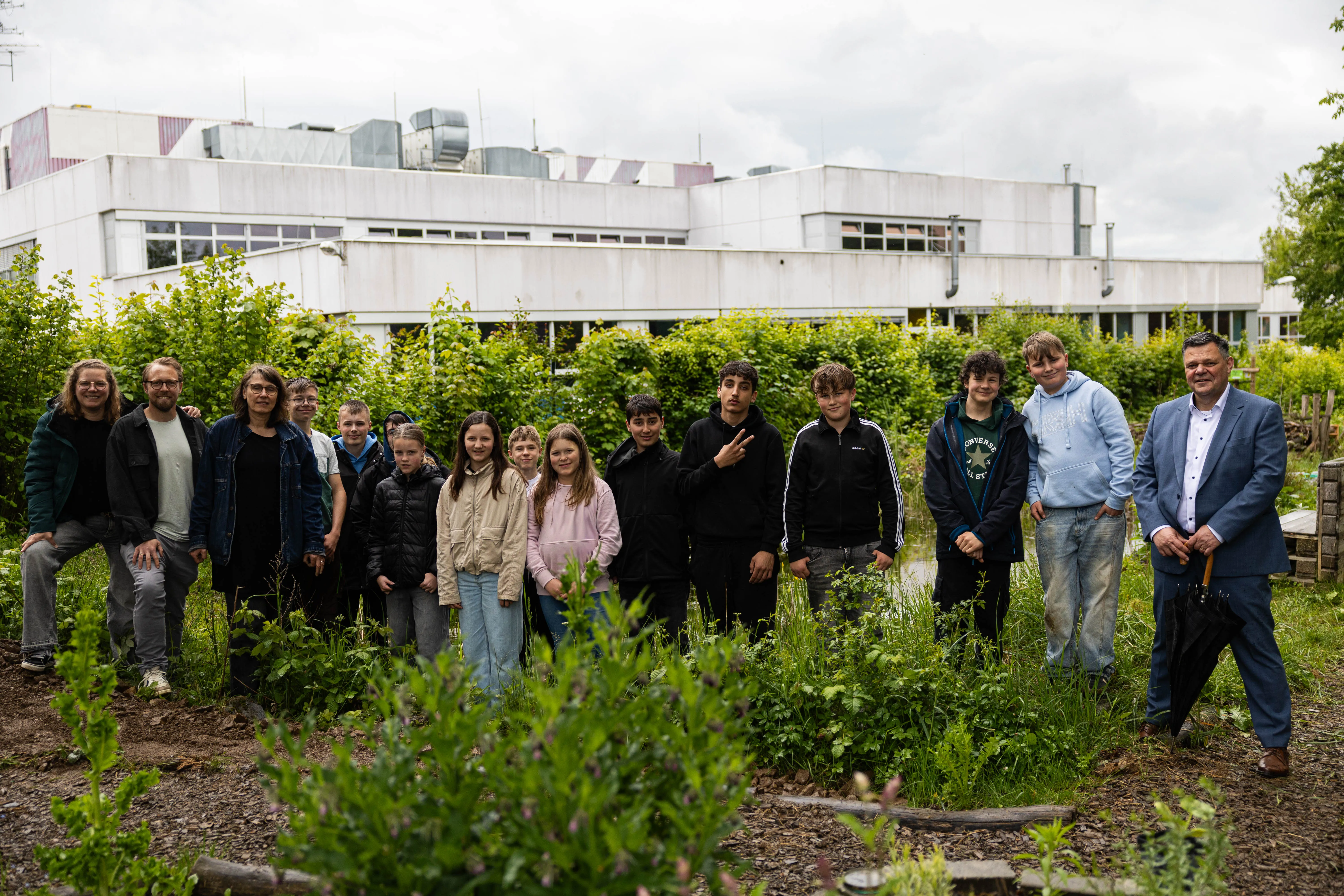 Gruppe von Jugendlichen und Erwachsenen steht in einem Garten vor einem modernen Gebäude. Sie sind Teil eines Projekts zur Wildbienenförderung, das vom Rotary-Club gesponsert wird.