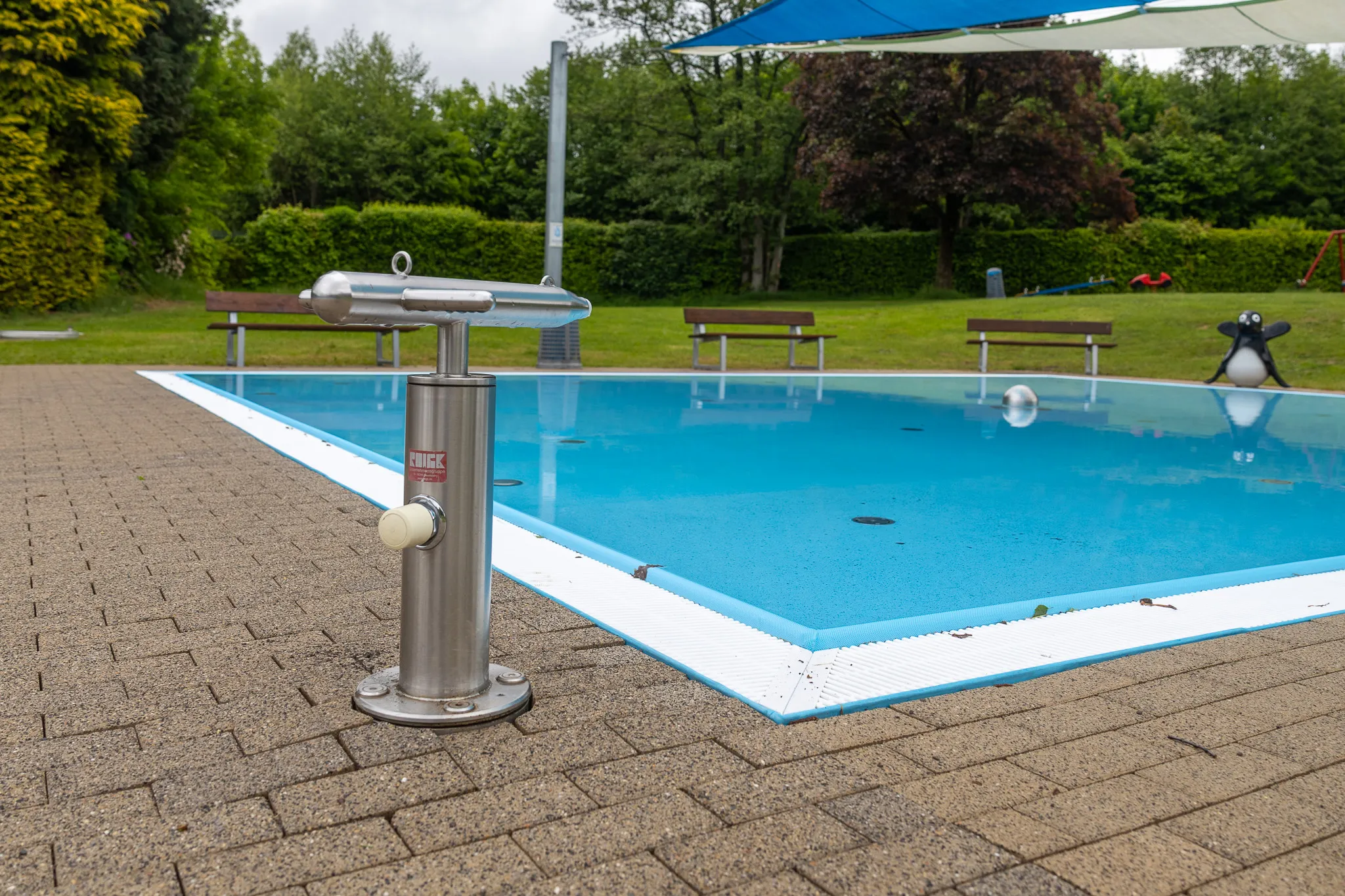 Edelstahl-Luftstation steht am Beckenrand eines blauen Schwimmbades mit Bahnenmarkierungen.