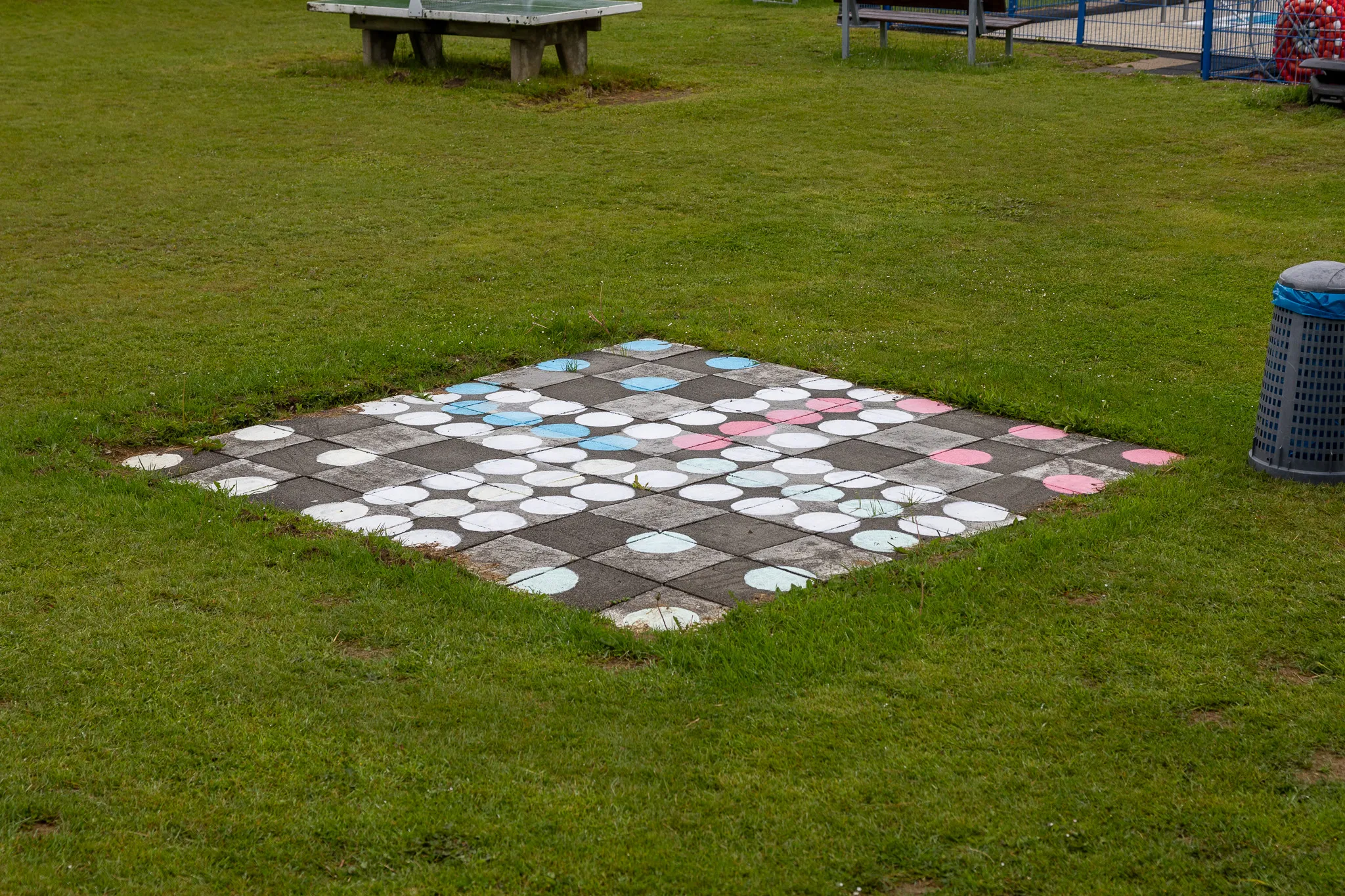 Quadratisches Spielbrett mit weißen und farbigen Kreisen auf einem Rasen im Freien.