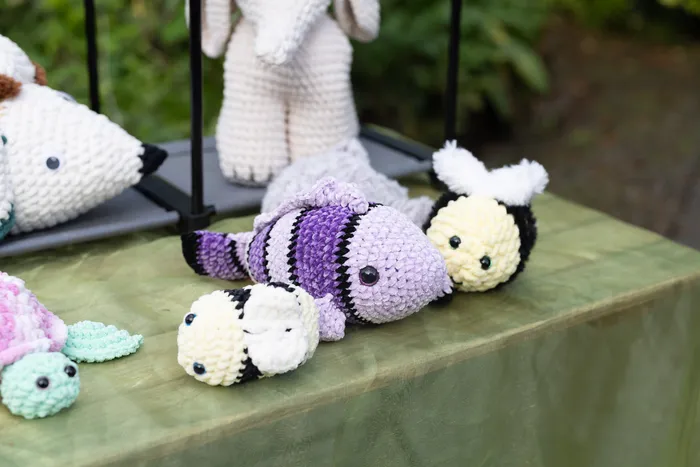 Verschiedene kleine, gehäkelte Tierfiguren wie ein lila Fisch und eine Biene liegen auf einem grünen Tuch.