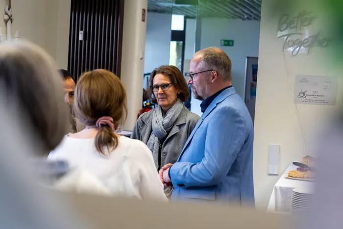 Drei Personen im Gespräch während des Ehrenamtstages im Jugendcafé Aquarium. Eine Frau mit grauen Haaren trägt eine Jacke und einen Schal, während ein Mann neben ihr einen blauen Blazer trägt.