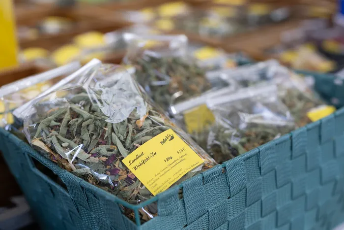 Durchsichtige Beutel mit getrocknetem Kräutertee, beschriftet mit „Landlust Wohlfühl-Tee“, liegen in einem grünen Korb.