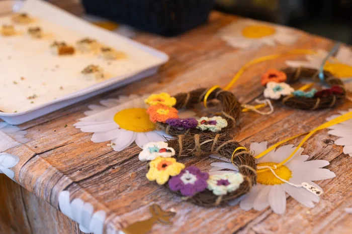 Kleine Zweigenkränze mit bunten Häkelblüten auf einem Holztisch mit Gänseblümchen-Muster.